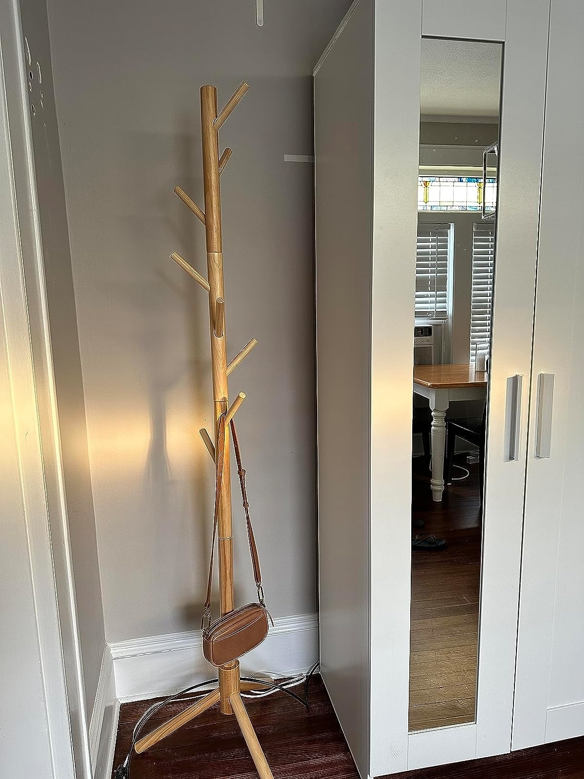Reviewer image of the light wood coat rack with a bag hanging on it in the corner of a room