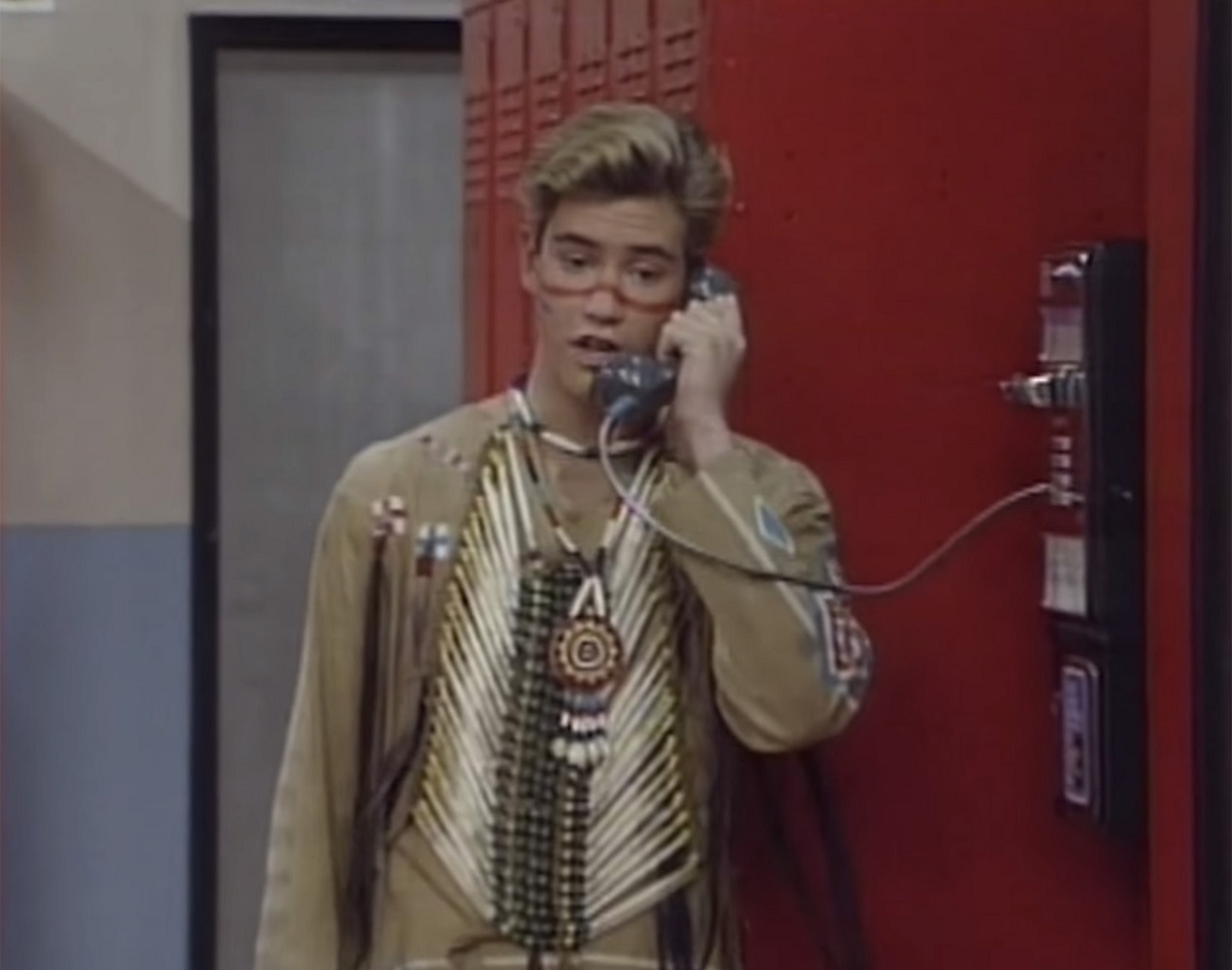 zach using a payphone while dressed up in the native american clothing