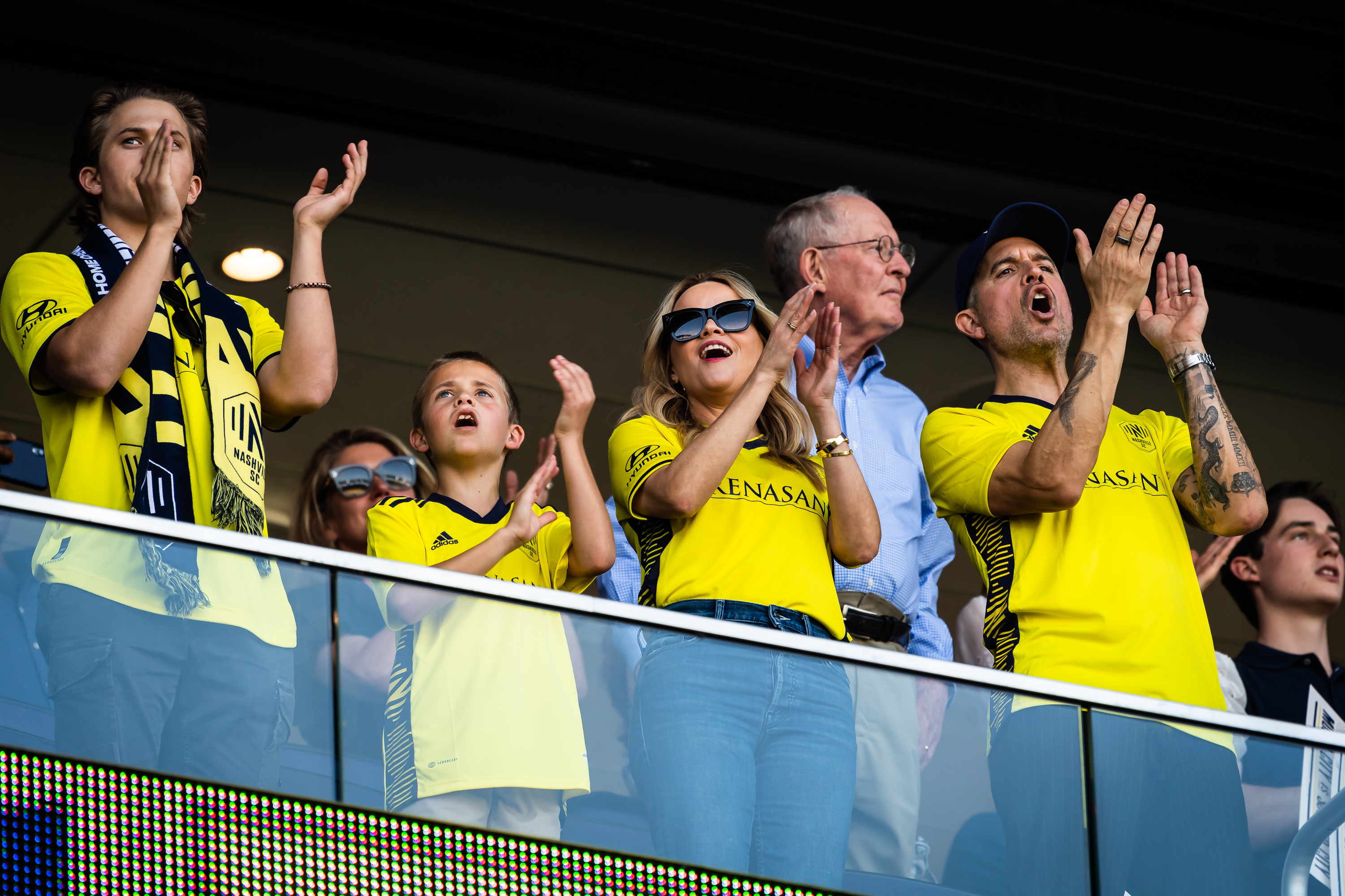 A family wearing yellow jerseys cheer during a soccer game.