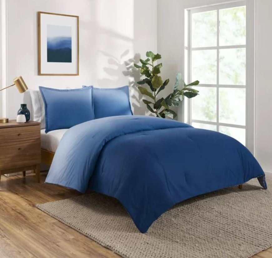 blue ombre bedding set with pillows in a bedroom with a nightstand, standing plant and rug underneath