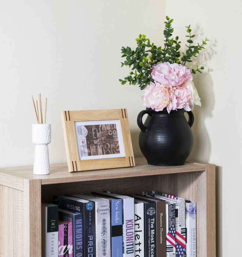 black vase with pink flowers sitting on top of a book shelf next to a picture frame