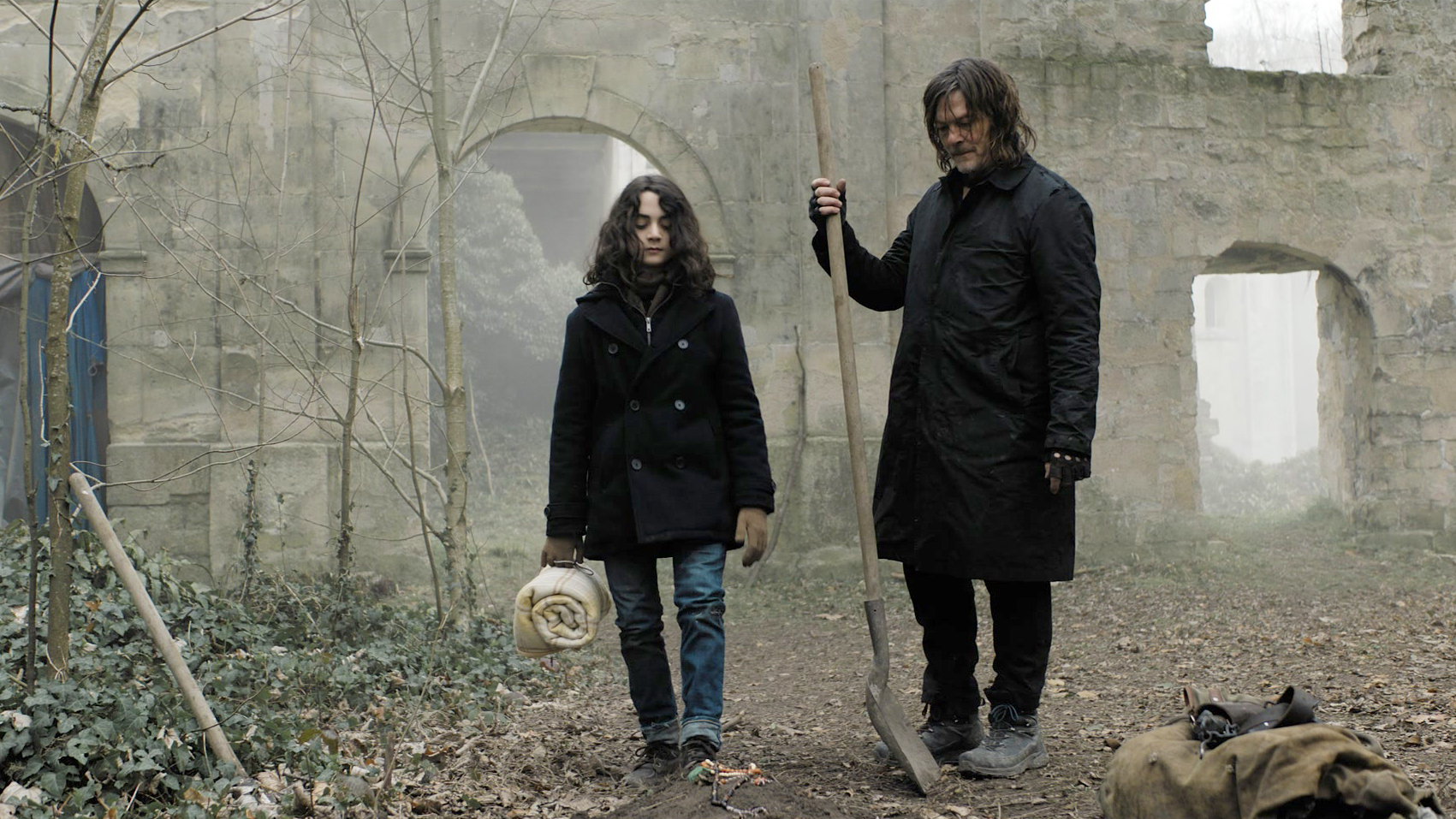 Daryl standing with a young person amid ruins