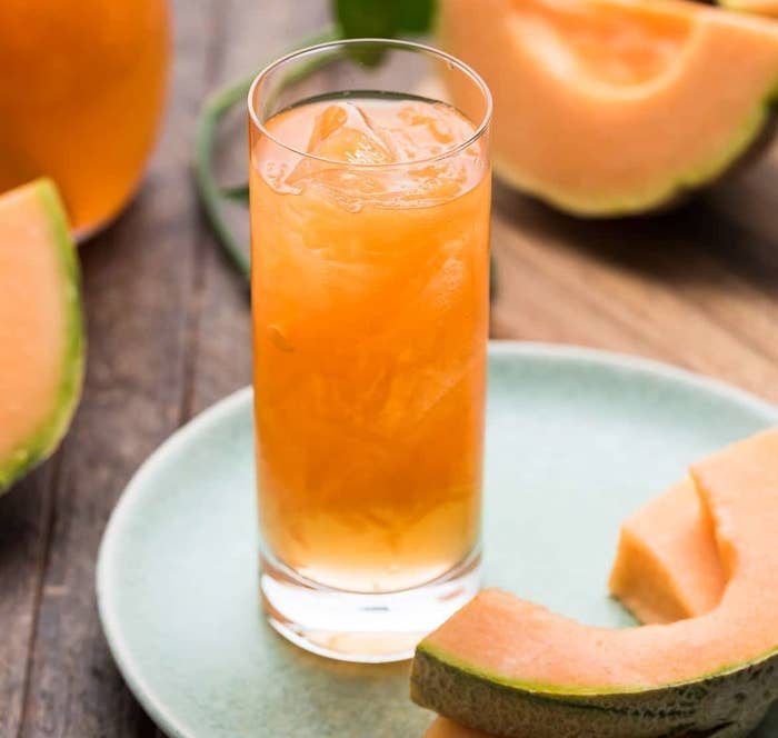 A glass of Melon is surrounded by cantaloupe rinds