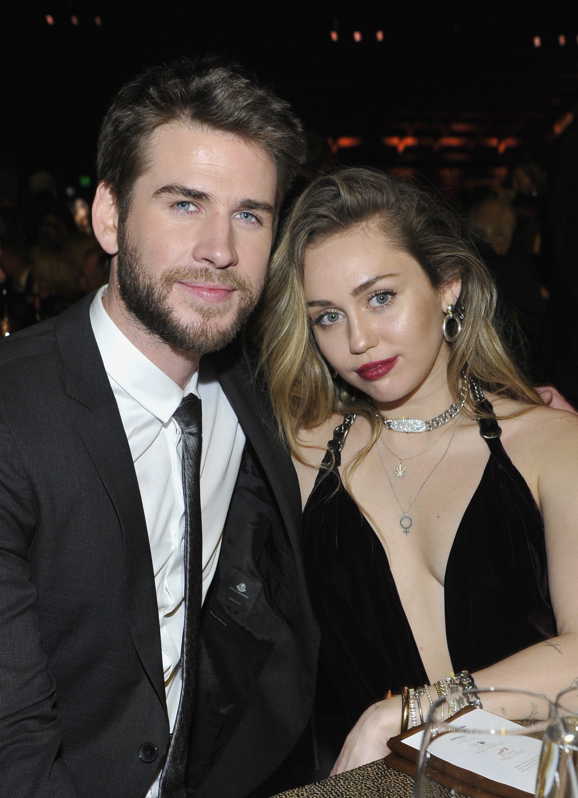 Liam Hemsworth and Miley Cyrus lean into each other as they pose for a photo at an event