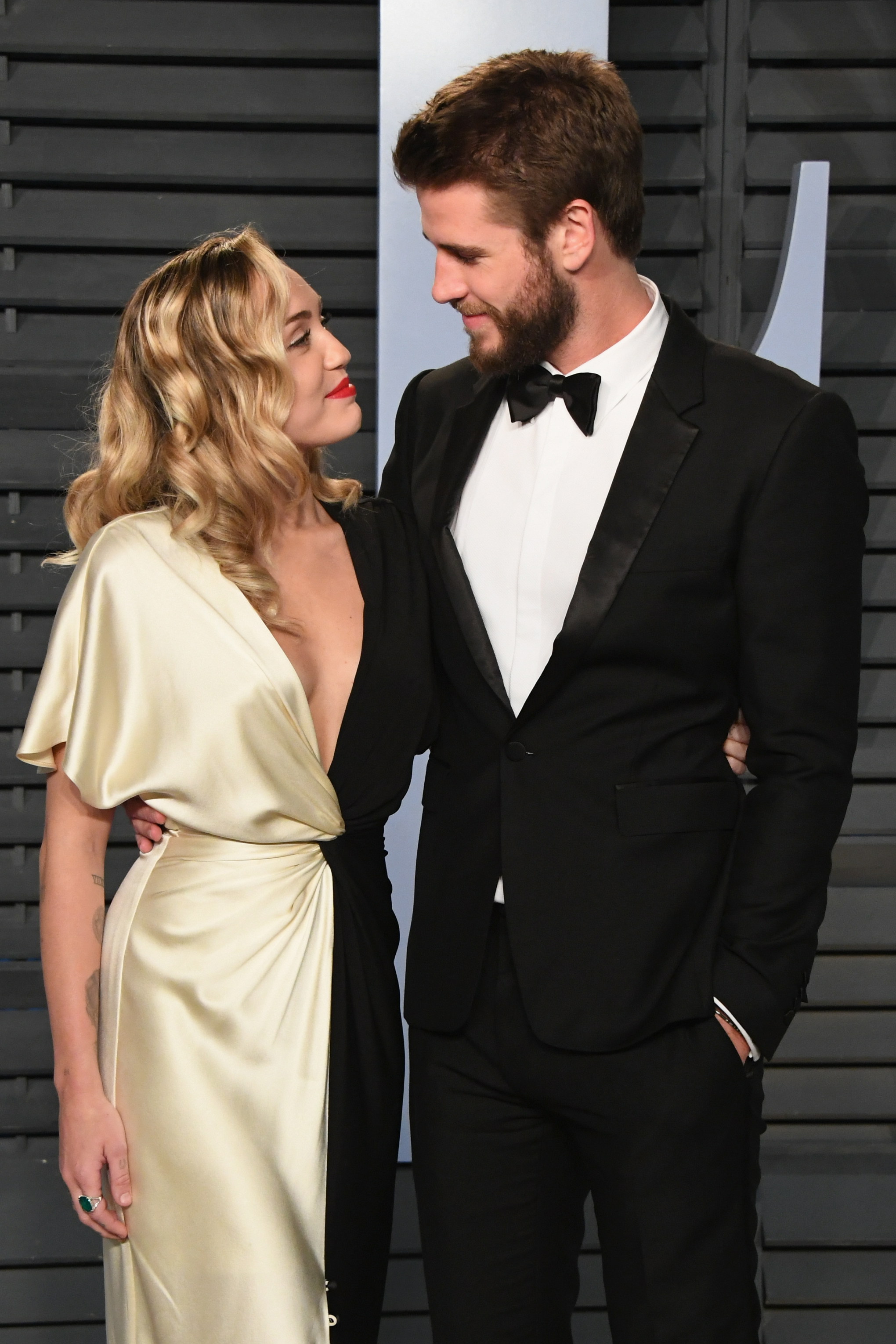 Miley Cyrus and Liam Hemsworth look at each other lovingly as they stand on the red carpet