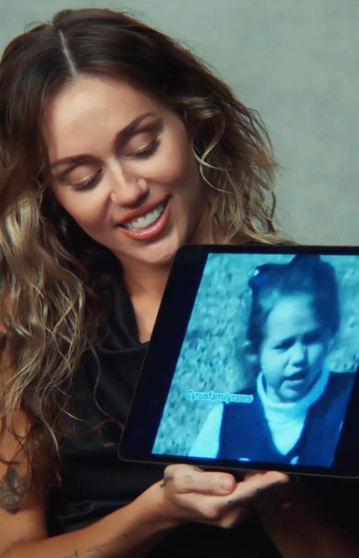 Miley Cyrus holding up an iPad that shows a photo of her as a toddler