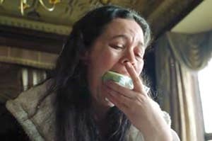 Olivia Colman eating a slice of cake with her hands as Queen Anne in The Favourite