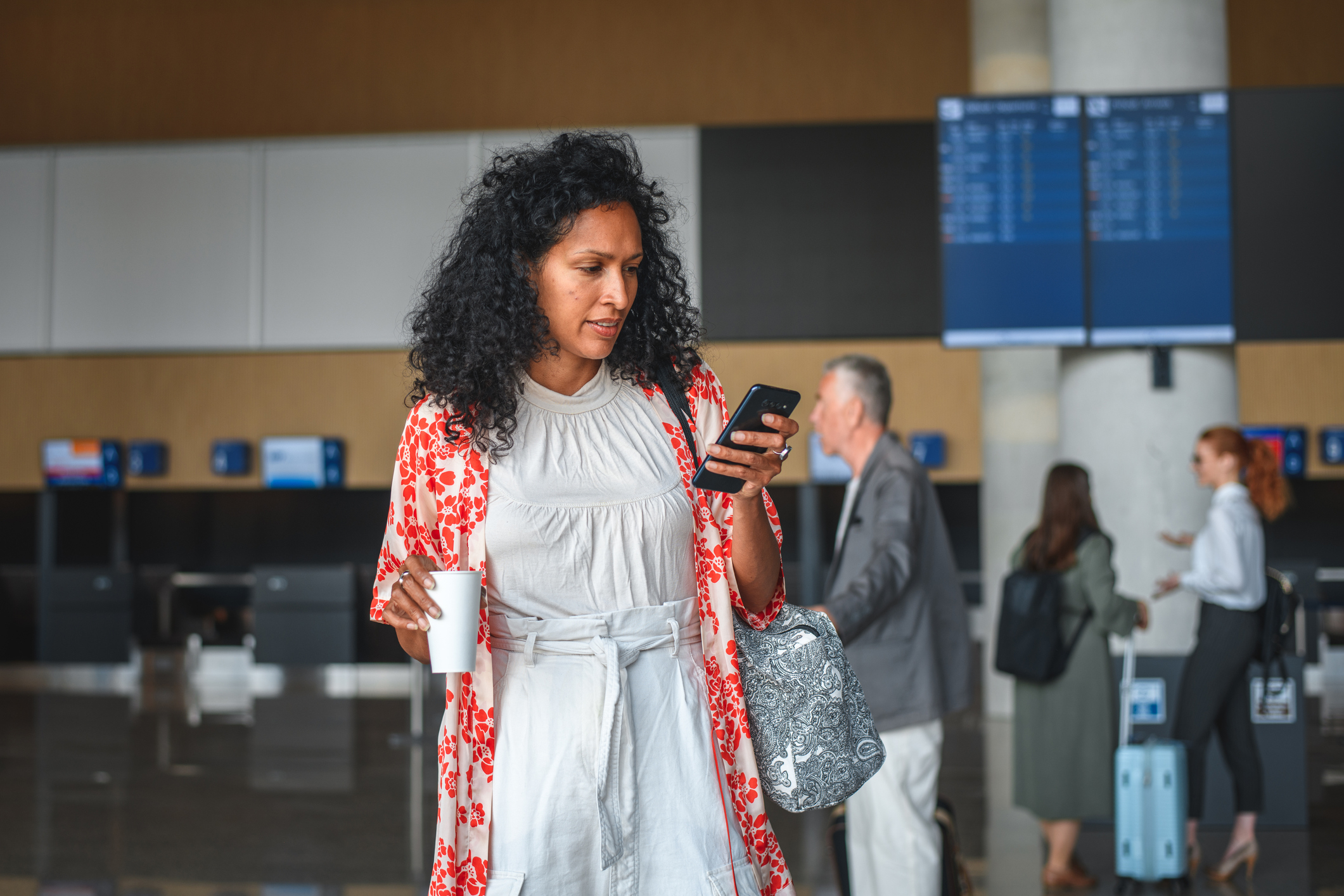 woman holding a phone and coffee at the airport