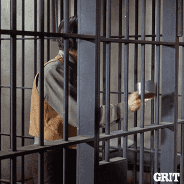 A man in a holding cell running a metal cup against the bars