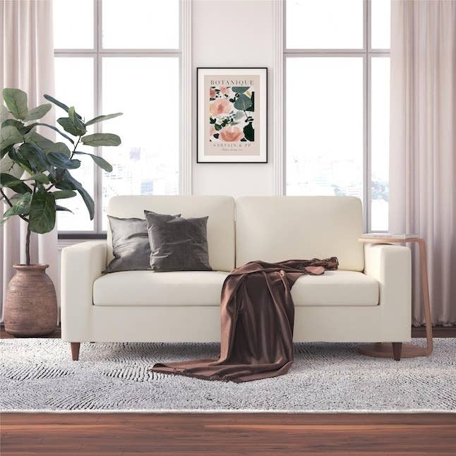 A white linen sofa in a living room with a carpet and plant.