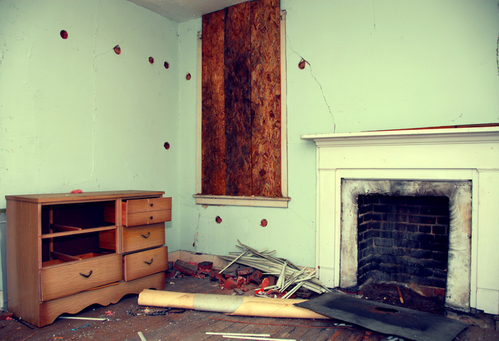 A trashed room of a house with a boarded up window