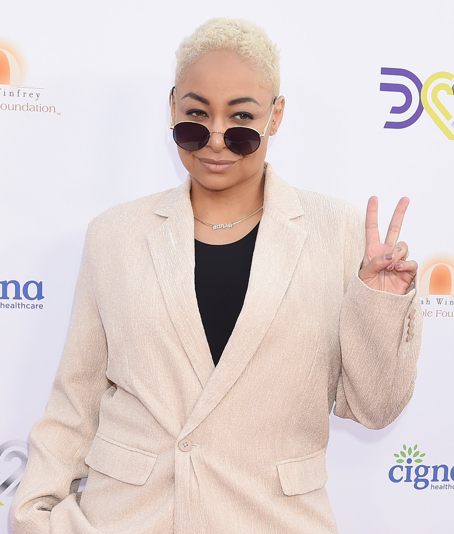 Raven in a blazer and sunglasses and giving the peace sign