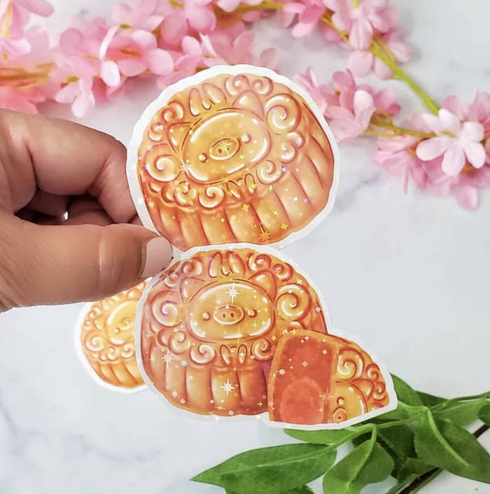 Hand holding glistening mooncake stickers with pig design.