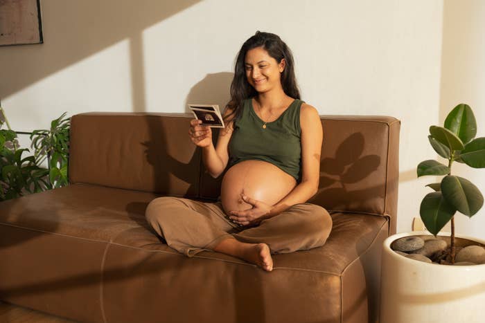 A pregnant woman is sitting on the couch looking at her ultrasound pictures