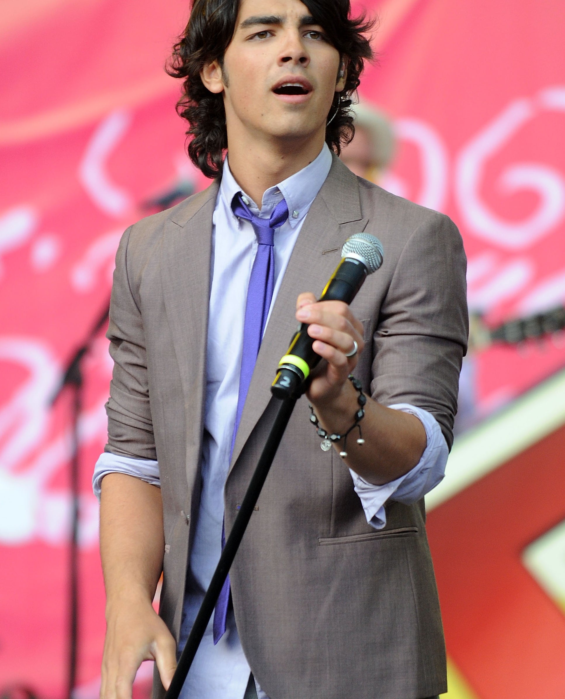 Joe Jonas performing onstage in a loose suit and tie