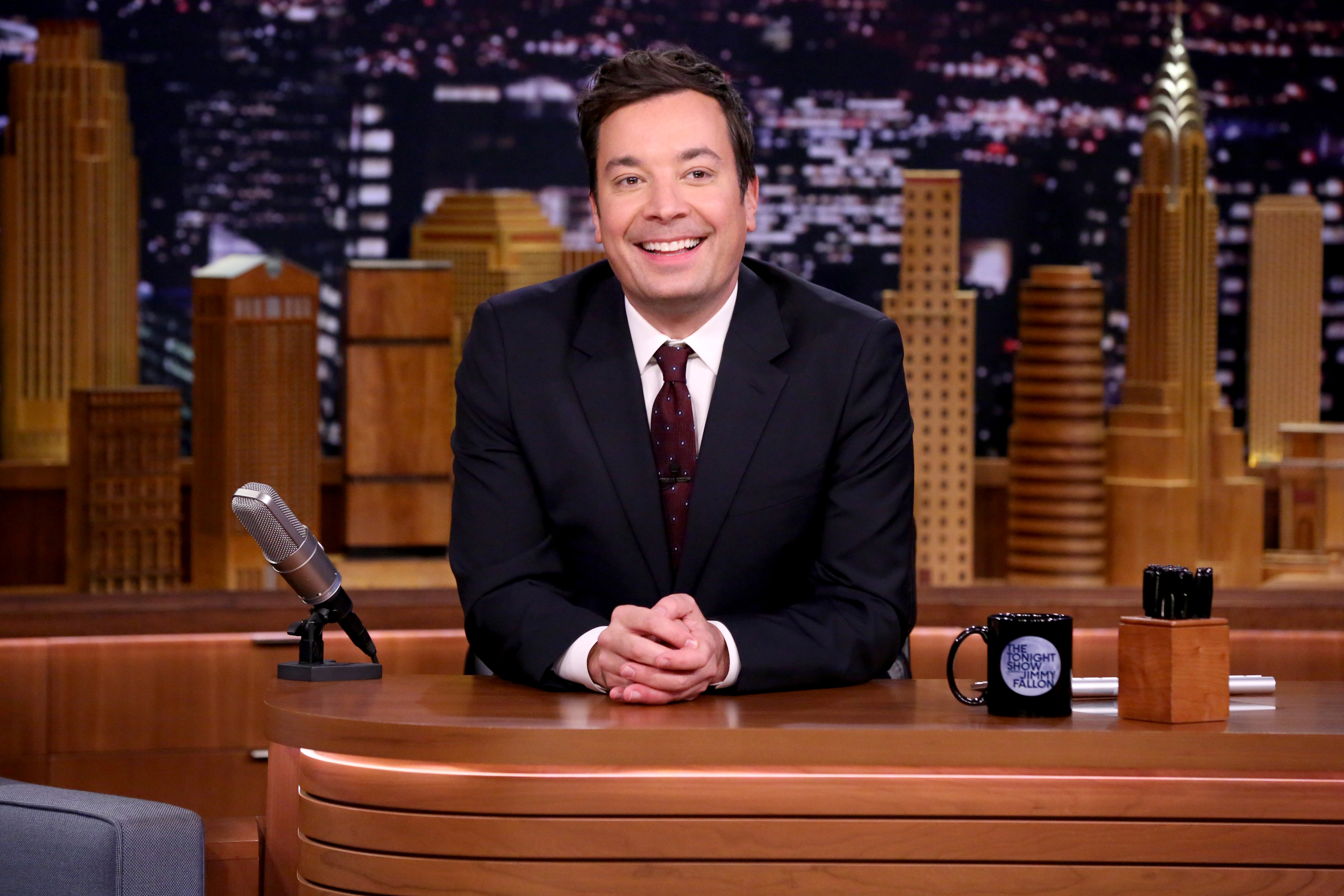 Jimmy Fallon smiles as he sits at his desk during his late night show