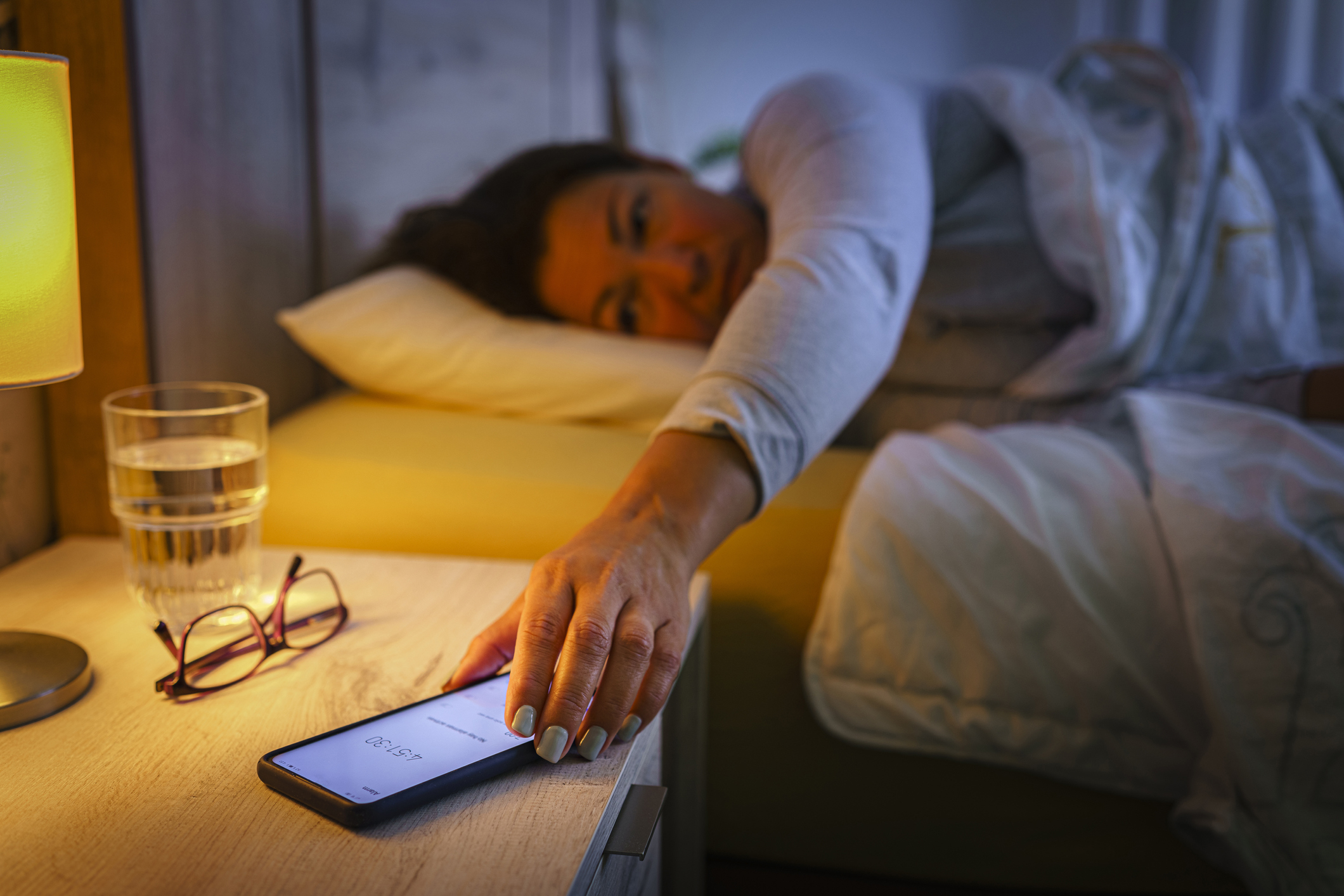 A woman in bed reaching for her phone
