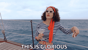 A woman standing on a yacht with a drink in her hand saying, &quot;this is glorious&quot;