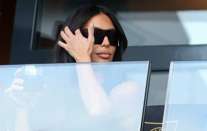 A closeup of Kim Kardashian wearing sunglasses and holding a drink