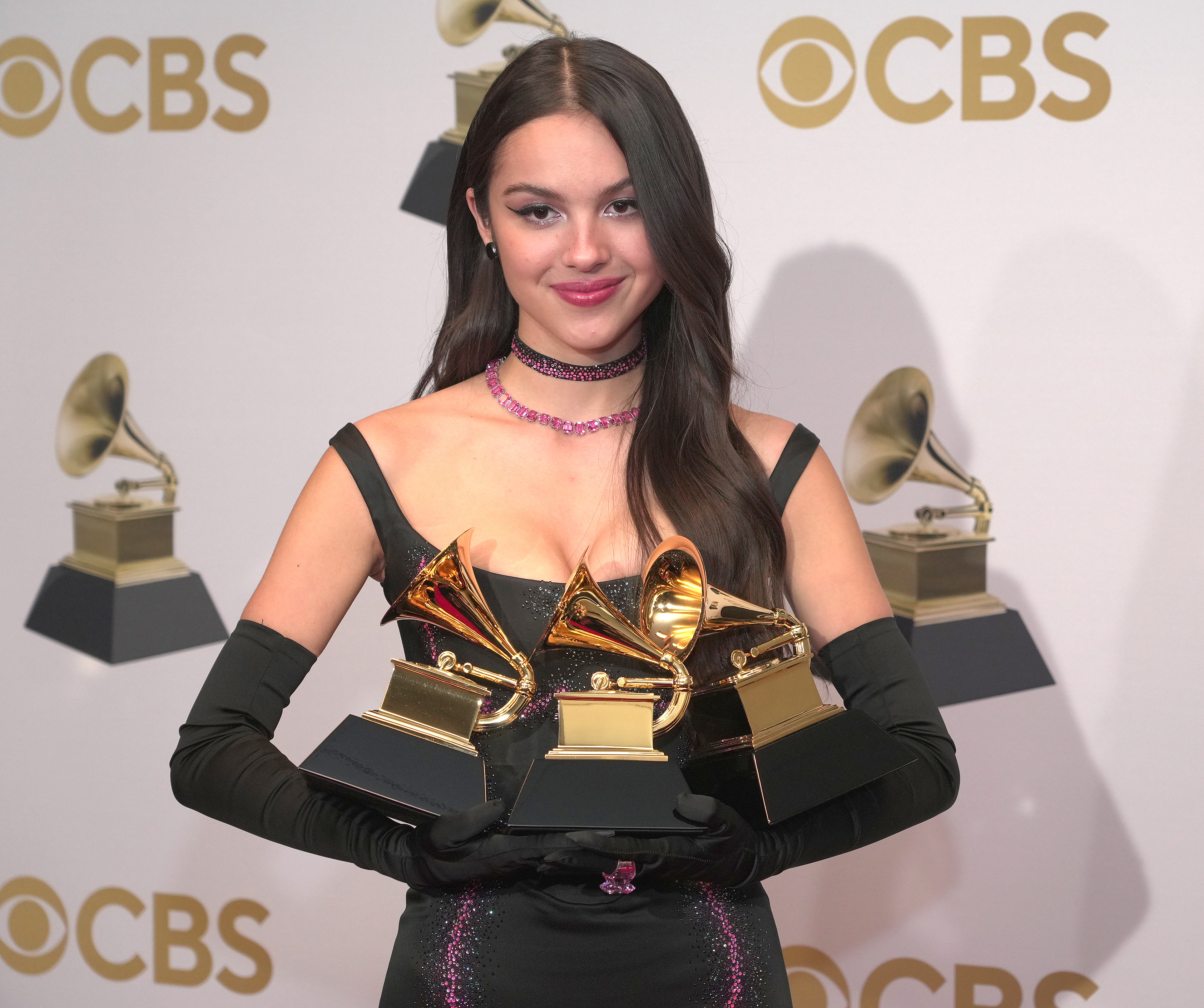 Olivia Rodrigo smiling and holding her three Grammy Awards backstage at the awards show