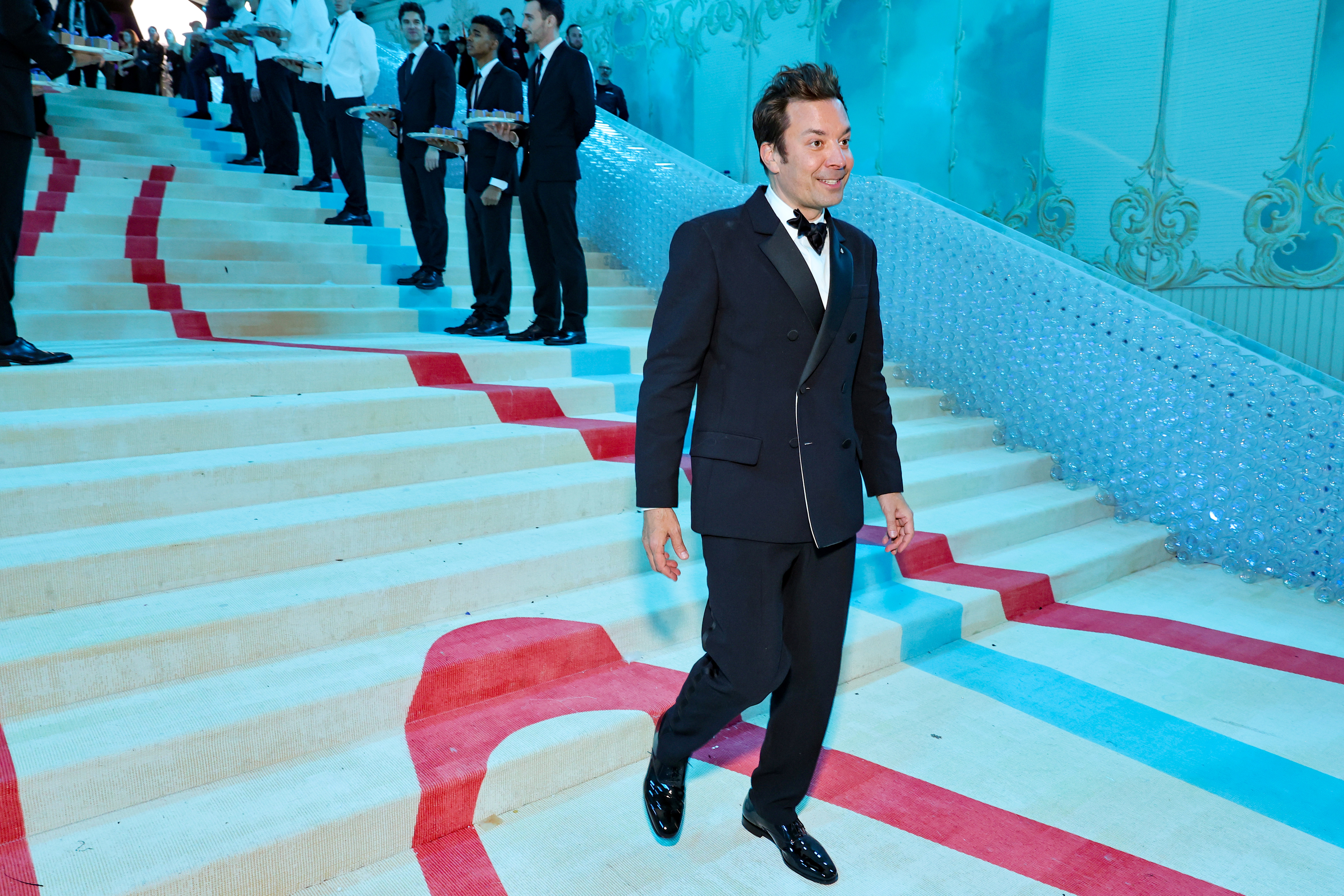 Jimmy Fallon walks down a set of grand stairs at formal event