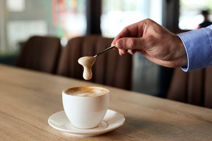 A cappuccino on a table as someone lifts foam out of the cup