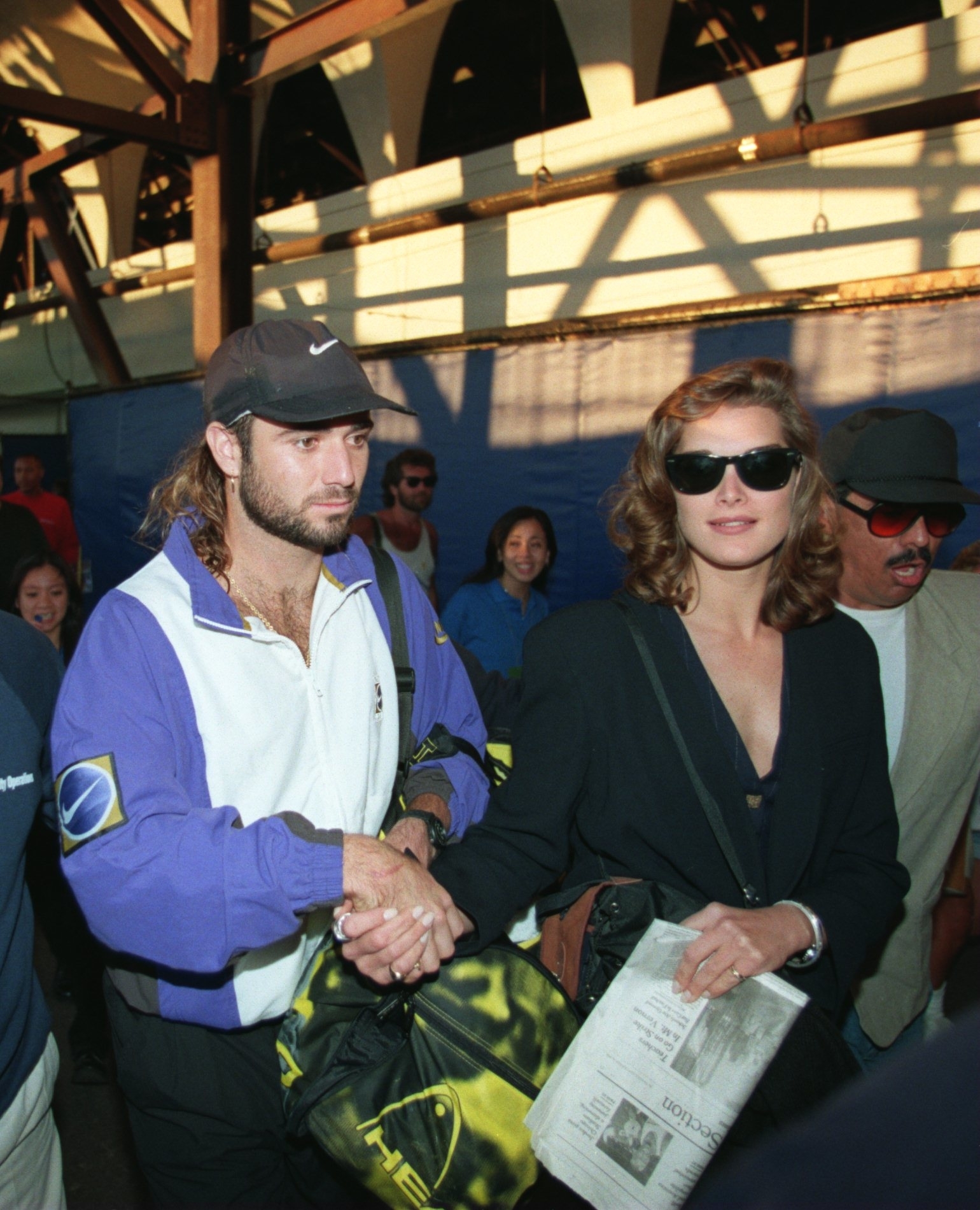 Brooke Shields and Andre Agassi hold hands as they walk through a crowd; he&#x27;s wearing a Nike cap and jacket and she&#x27;s wearing sunglasses
