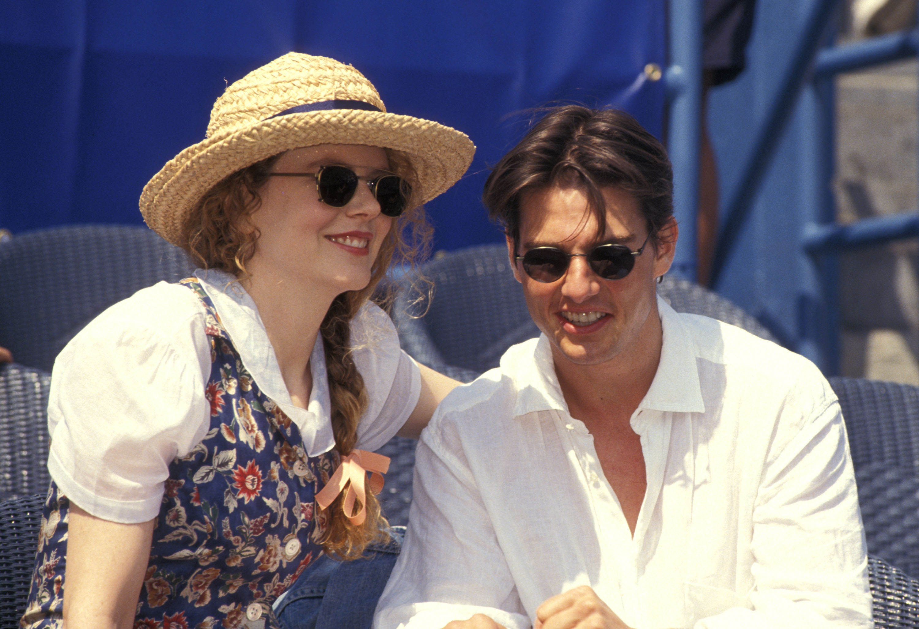 Nicole Kidman and Tom Cruise smile as they sit next to each other; they&#x27;re both wearing sunglasses and she&#x27;s wearing a straw sun hat