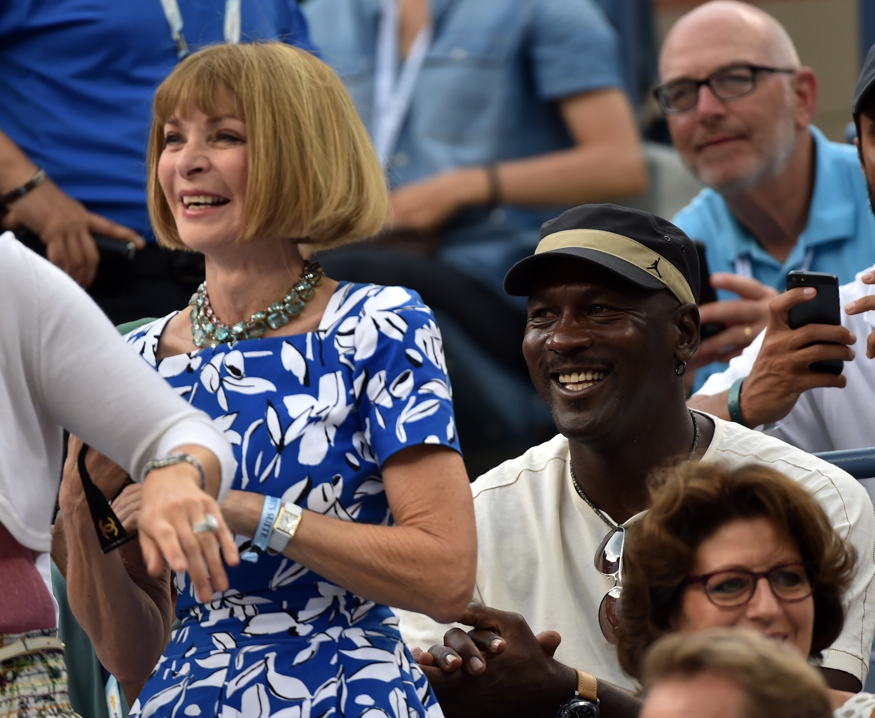 Anna Wintour smiles as she stands at her seat while Michael Jordan applauds and smiles while sitting