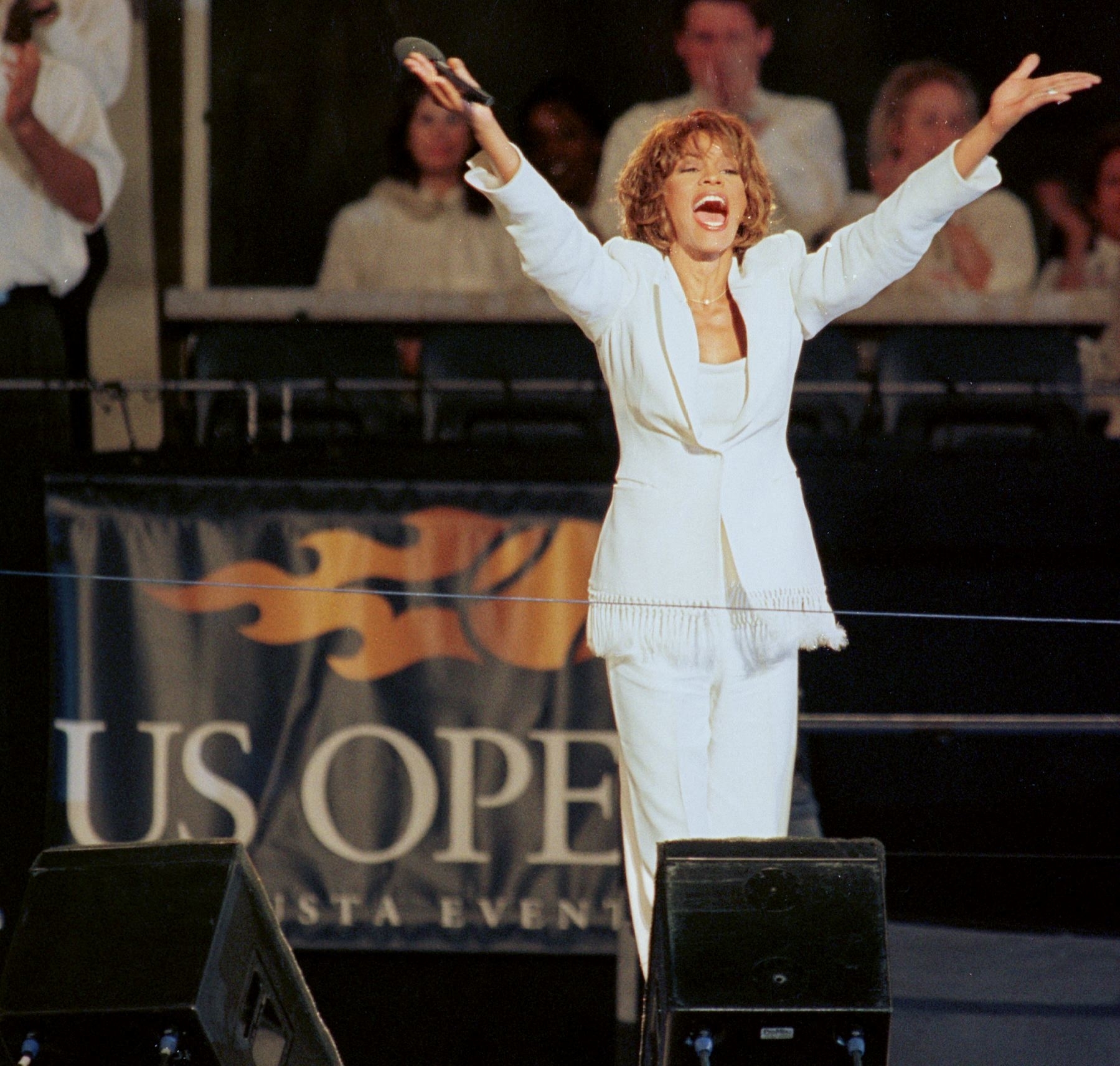 Whitney Houston stands onstage with her arms outstretched as she performs at the US Open