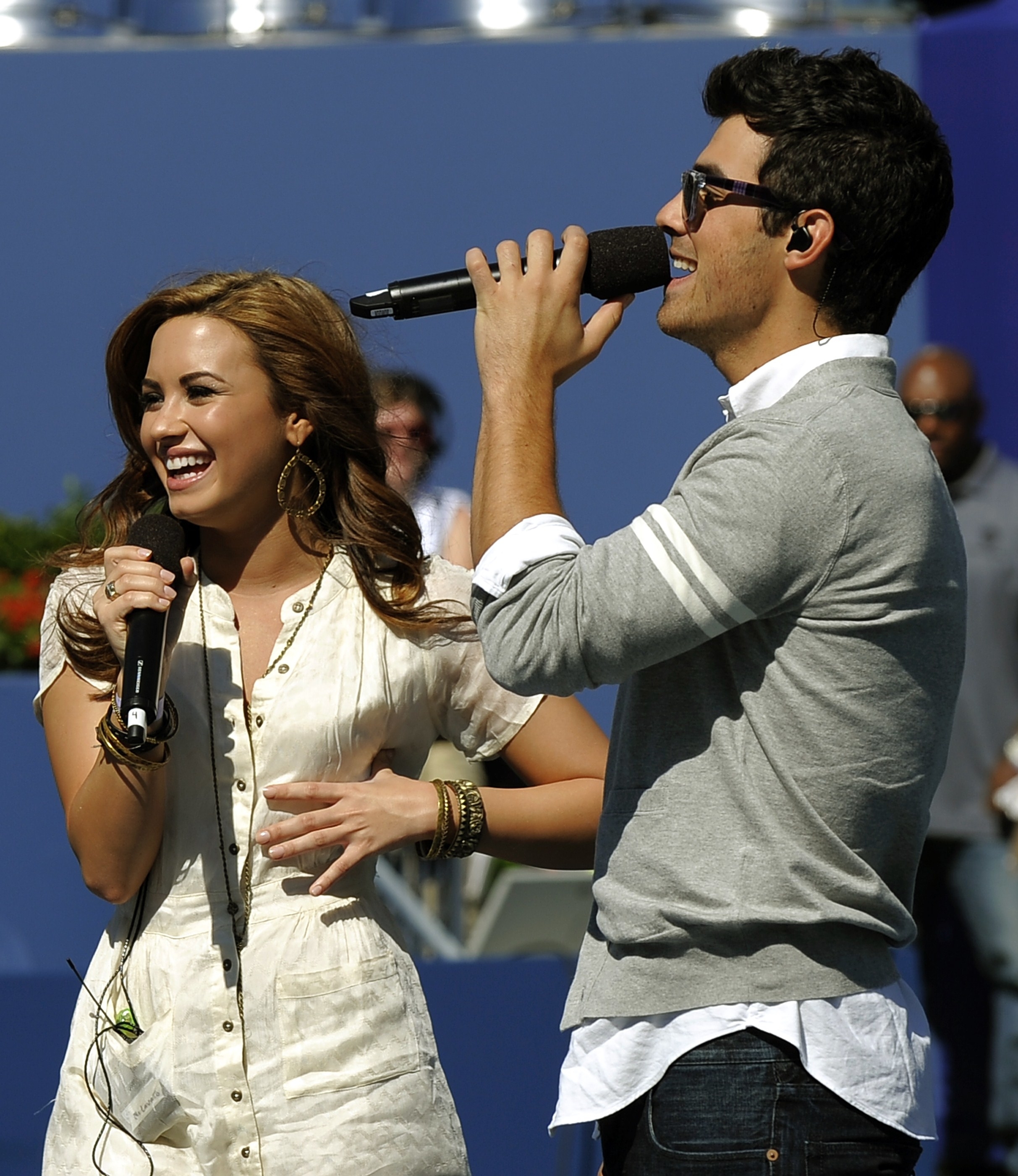 Demi Lovato and Joe Jonas holding microphones and performing together on the court at the US Open