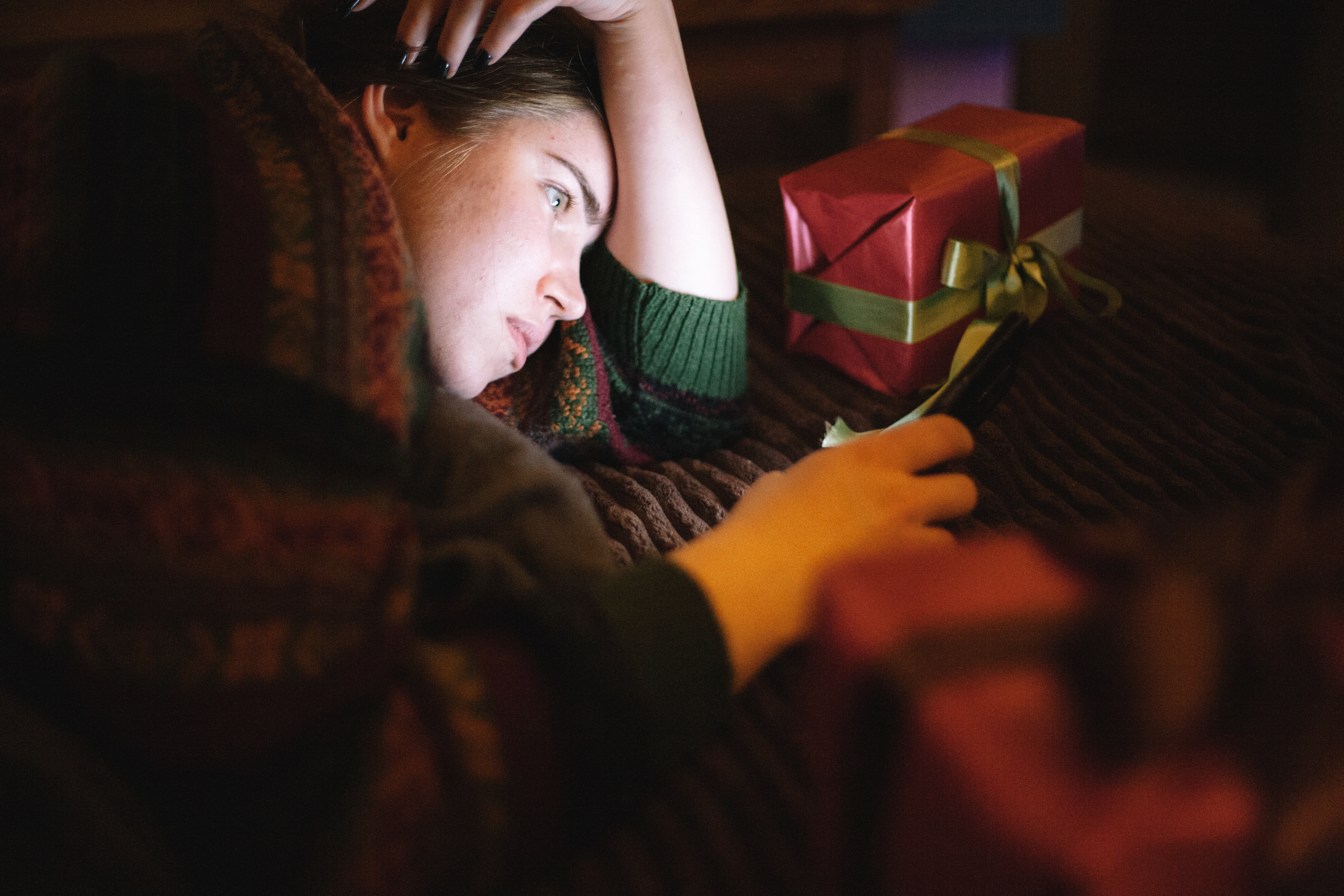 Young girl&#x27;s face illuminated by her phone while laying down.