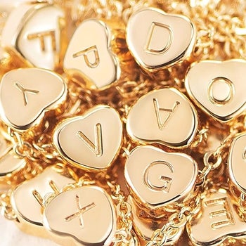 a pile of gold heart charms with initials engraved into each one