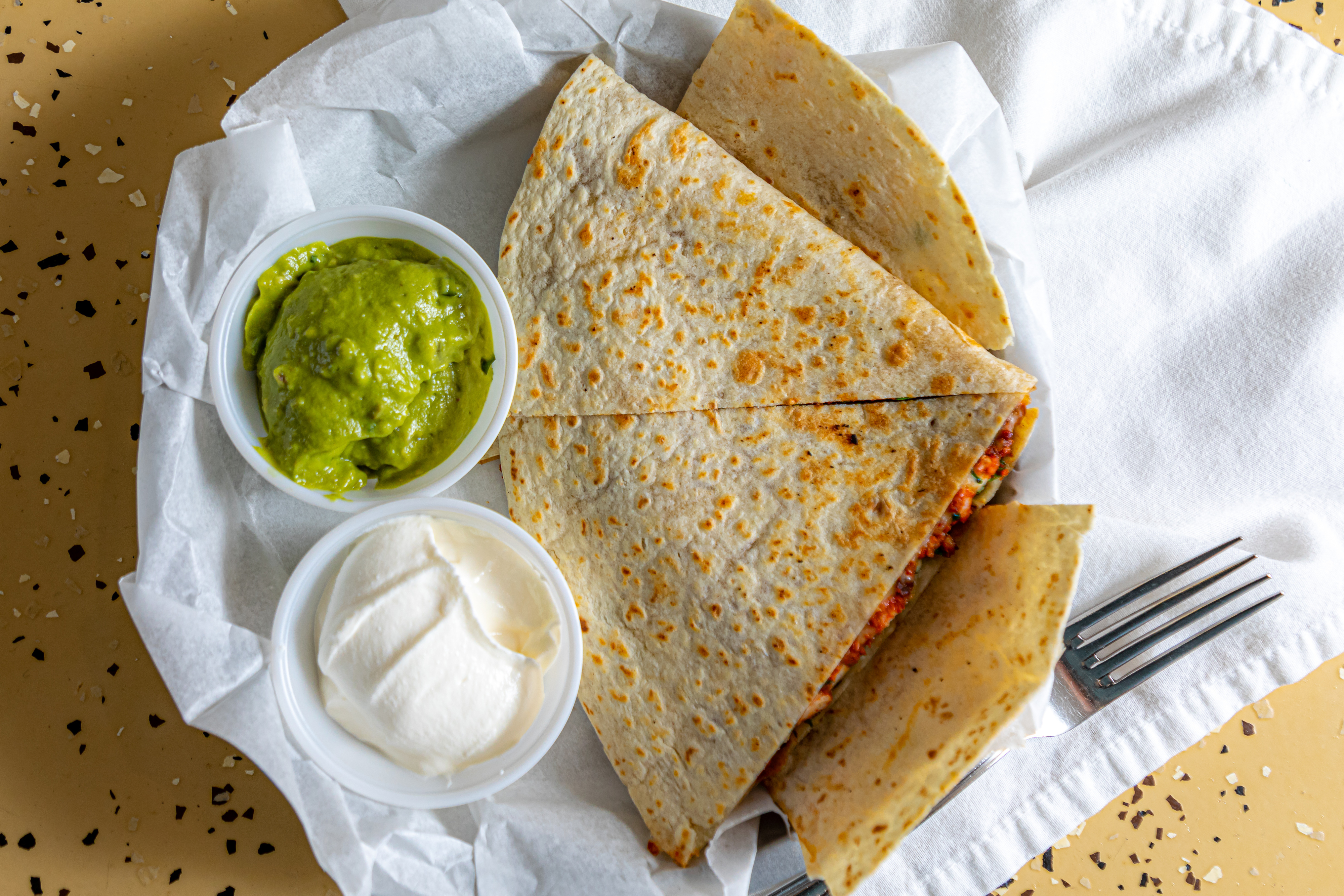 a quesadilla on a platter with guacamole and sour cream
