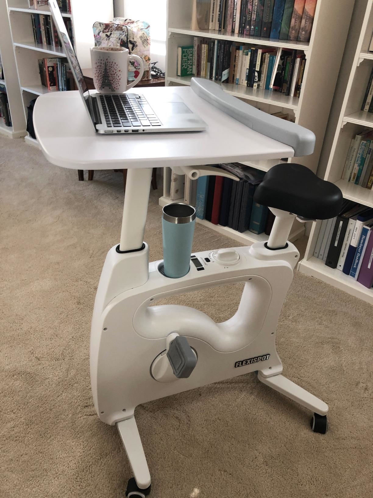 Reviewer image of white bike desk in a home with laptop propped on the tray and drink in the holder