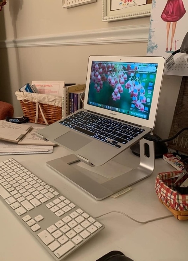 silver laptop stand with laptop above keyboard on desk