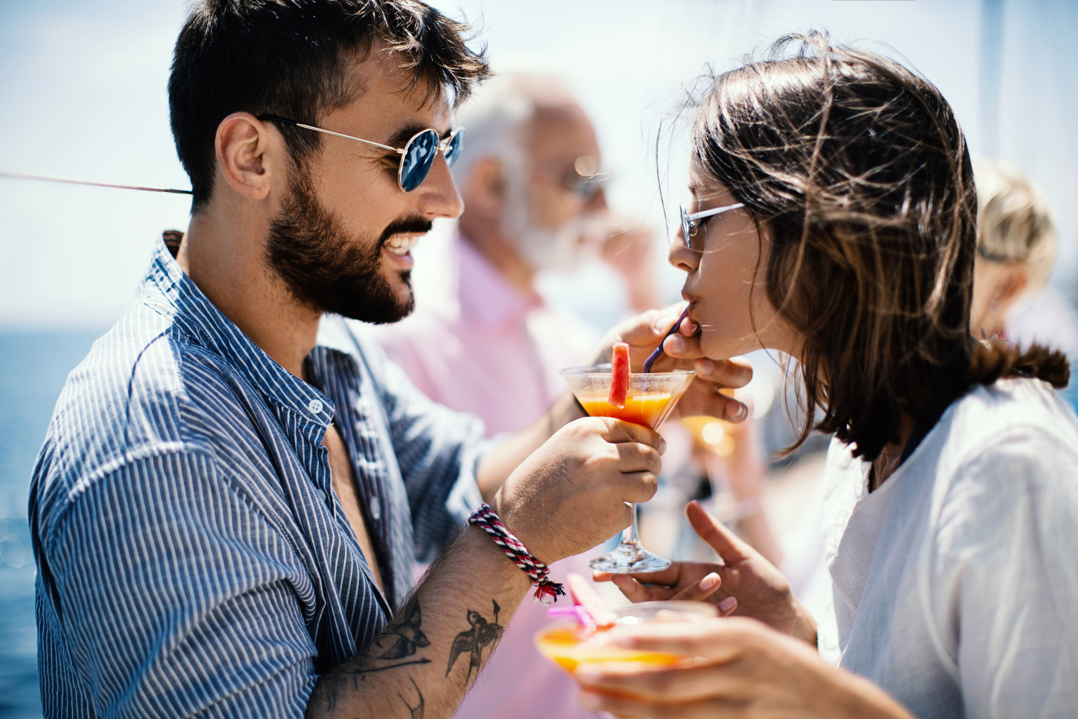 A man helping a woman take a sip of a fruity drink on a boat