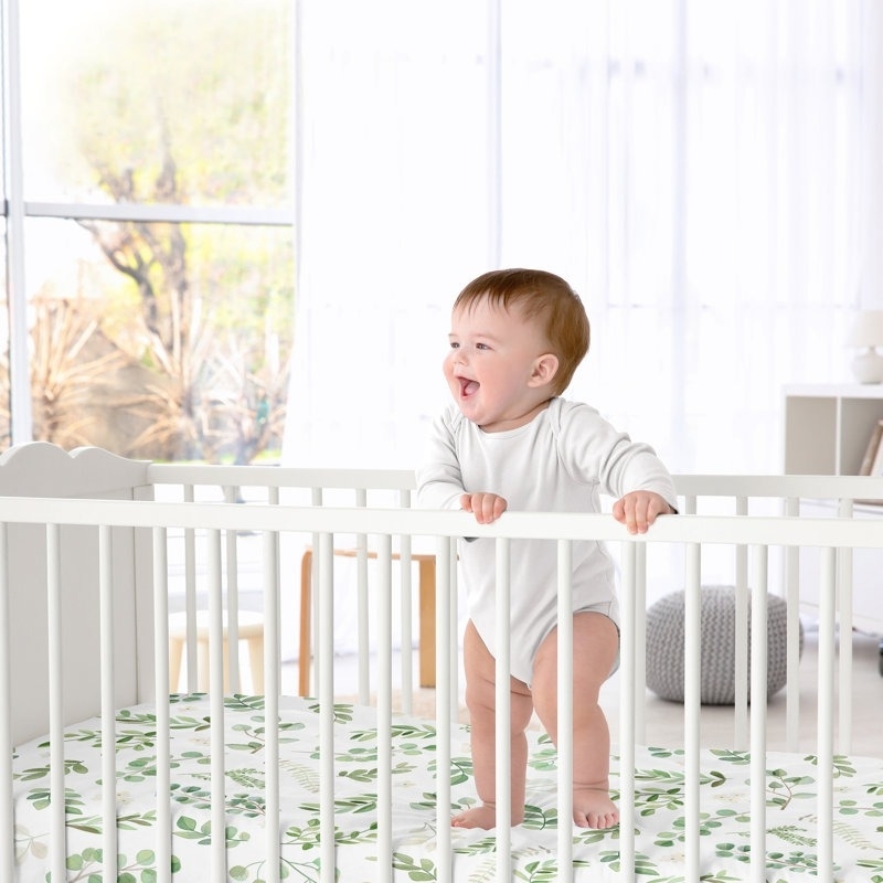 a baby standing on the green and white crib sheet