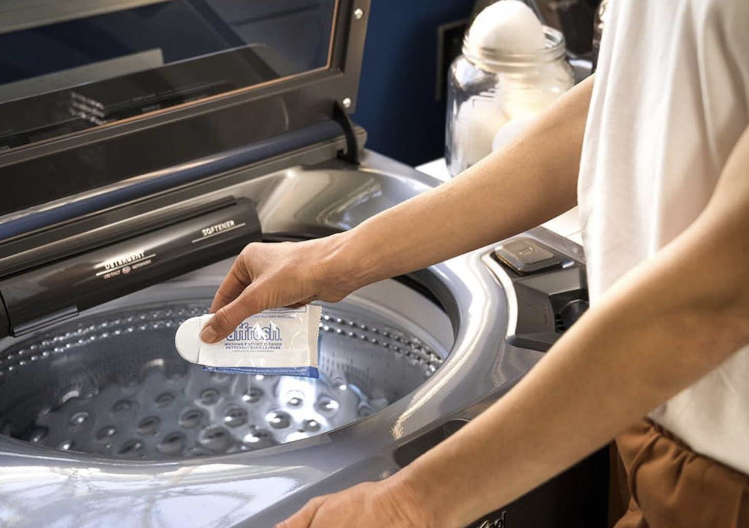 person putting a cleaning tablet into a top loading clothes washing machine
