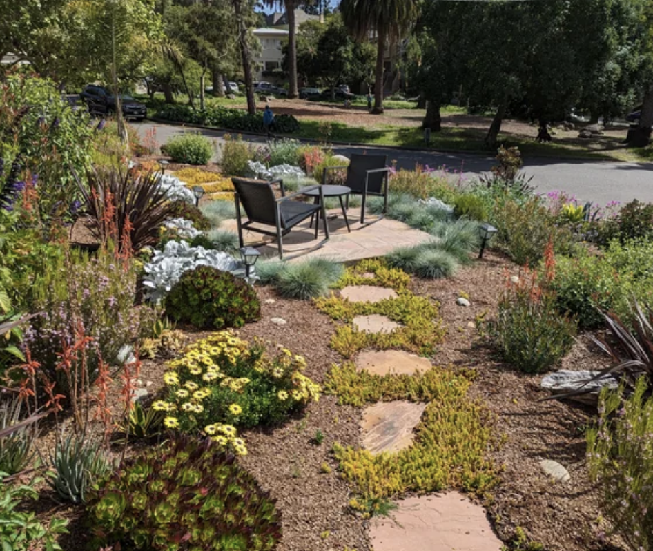 Someone&#x27;s yard that&#x27;s set up with a table and chairs, surrounded by plants and flowers