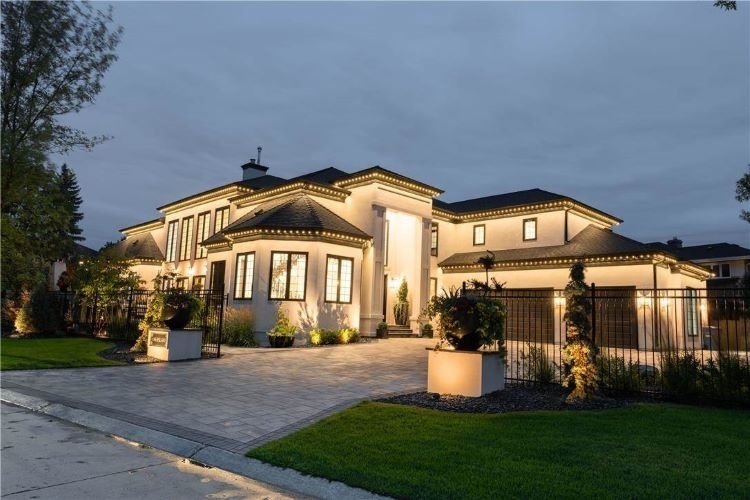 Gated home with high entrance way and triple car garage is illuminated at night.