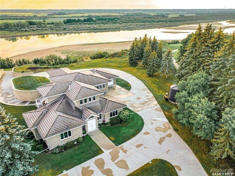 Large home backing onto river and flat green land.