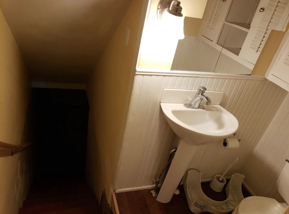 A dark stairway extending from a bathroom next to the sink and mirror