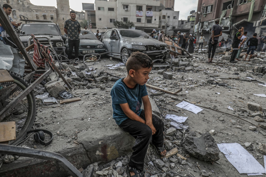 2023年10月10日、イスラエル軍による空爆を受けたガザ地区の都市ハーン・ユニスで、建物のがれきの中に座り込むパレスチナ人の少年（Getty Images）