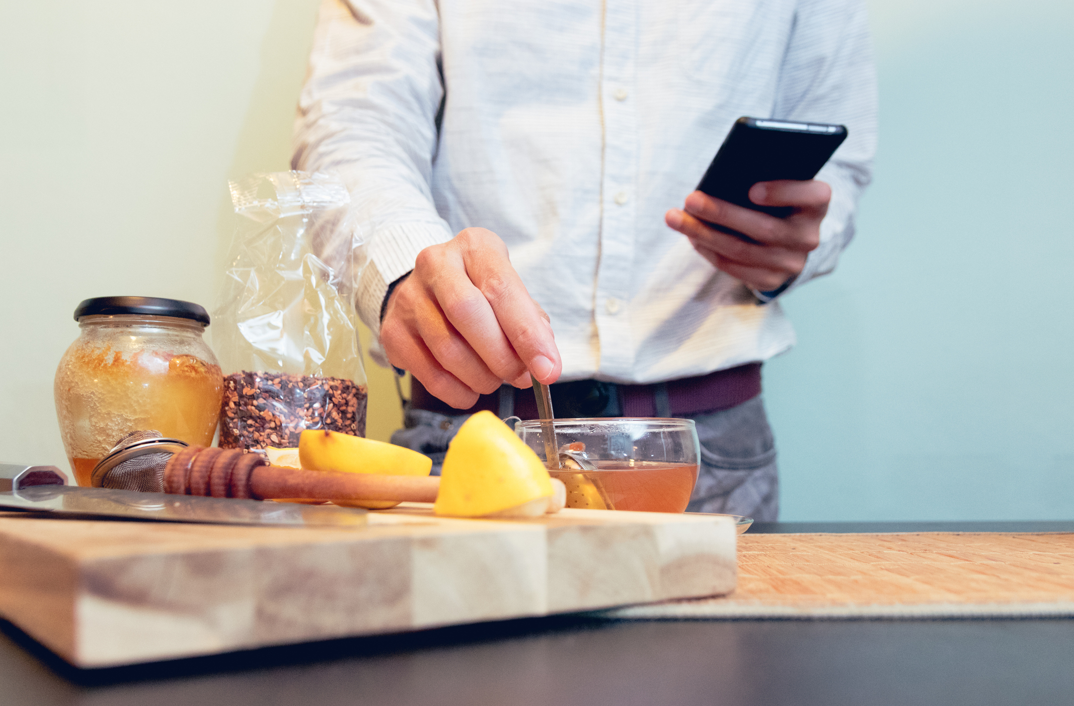 A man brewing tea while looking at his phone