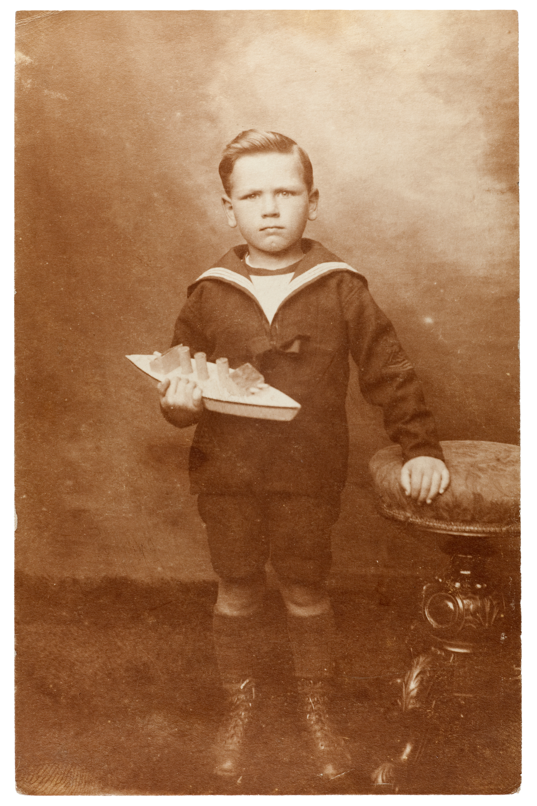 photo of a young boy in a sailor&#x27;s outfit holding a toy boat, circa 1910