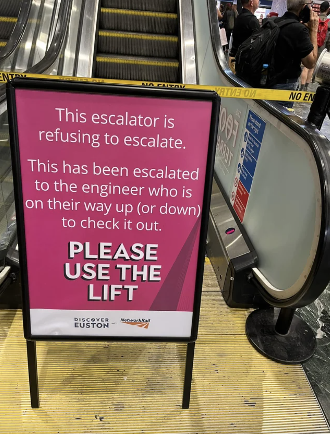 A sign next to an escalator says &quot;this escalator is refusing to escalate. This has been escalated to the engineer who is on their way up (or down) to check it out&quot;
