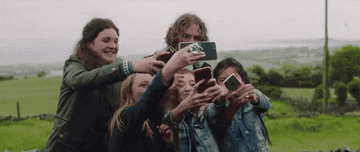 A group consisting of three kids and two older people are taking pictures on phones