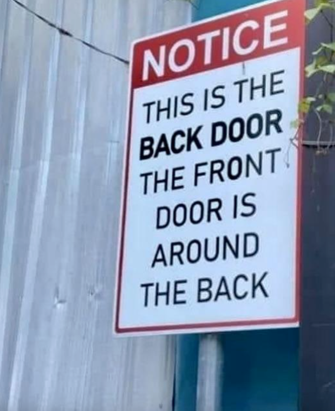 An installed sign says &quot;this is the back door, the front door is around the back&quot;