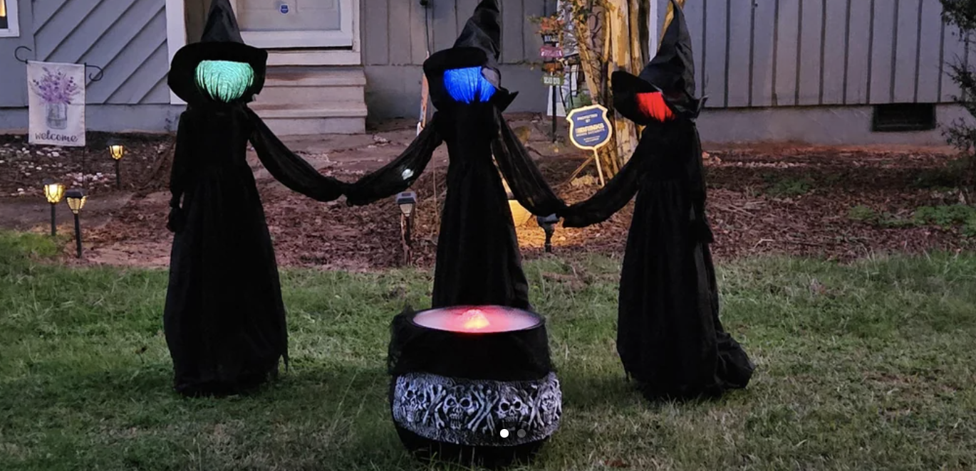 Three witch mannequins hold hands around a fake cauldron with a light inside it